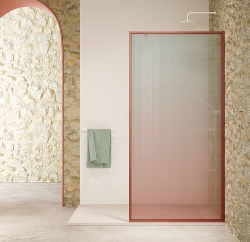 Ducha con puerta de vidrio de color descolorido, marco de coral, paredes de color pastel, una toalla verde y una pared de piedra arqueada.