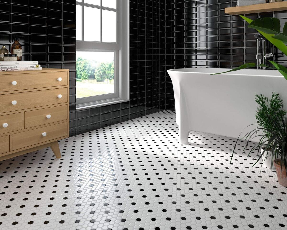 Baño con paredes de azulejos negros, bañera blanca, tocador de madera y piso estampado.