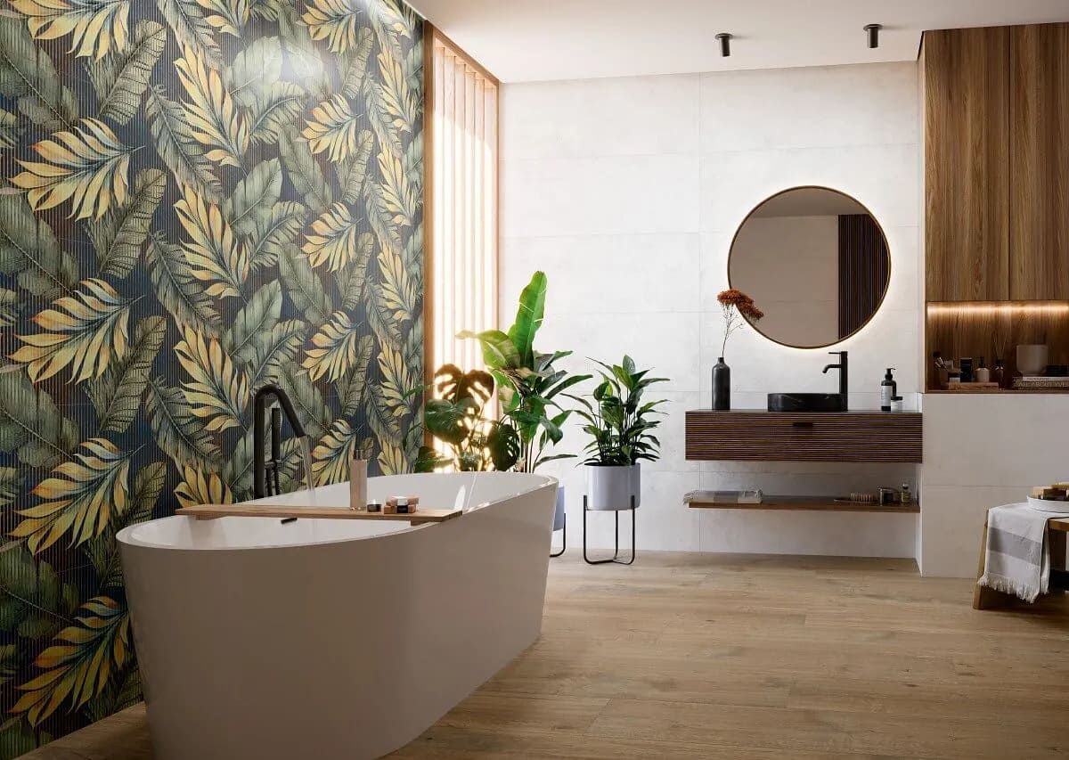 Baño con bañera independiente, pared decorativa con diseño de hojas, detalles de madera, espejo redondo y plantas.