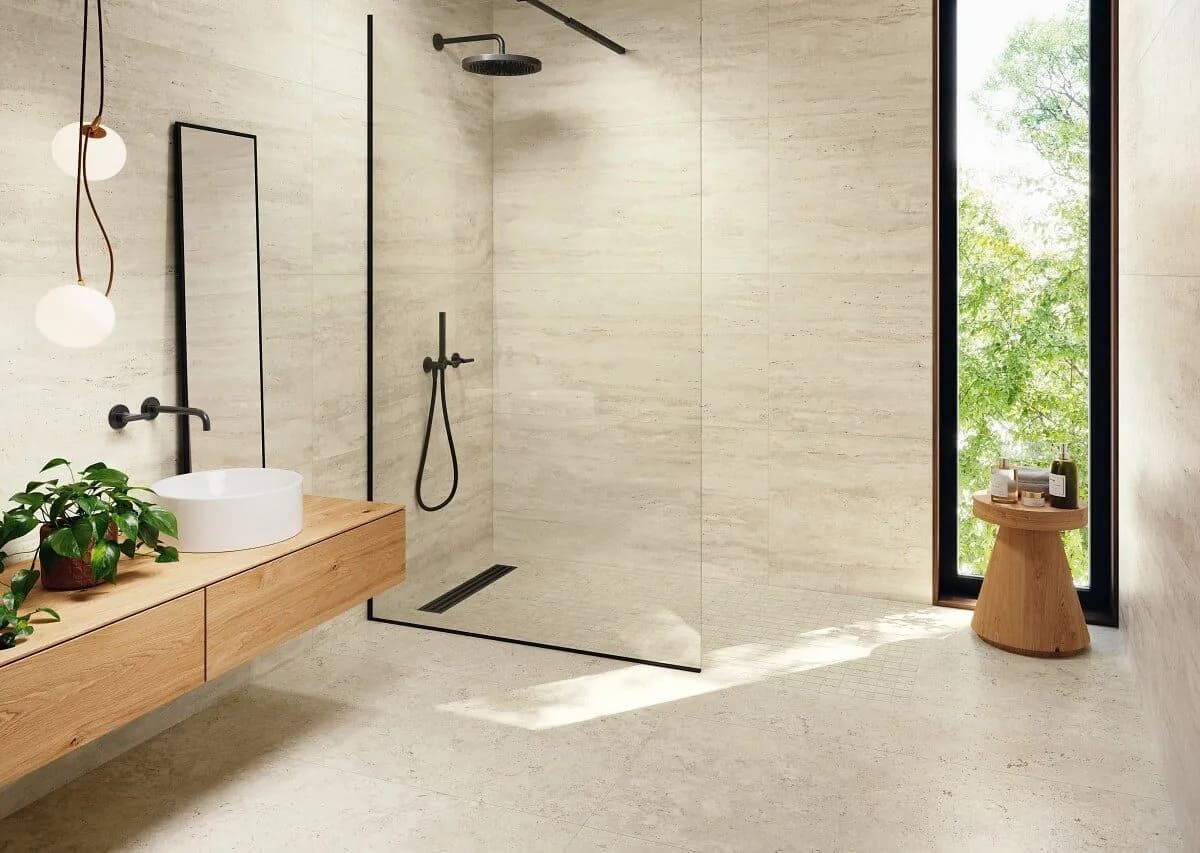 Baño moderno con ducha a ras de suelo, luz natural y tocador de madera clara.