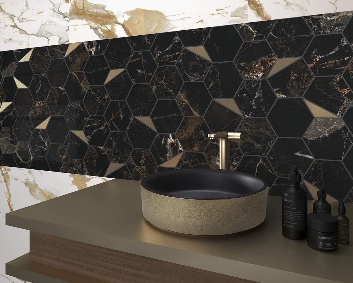 Baño con azulejos hexagonales negros y dorados, accesorios dorados y lavabo redondo.