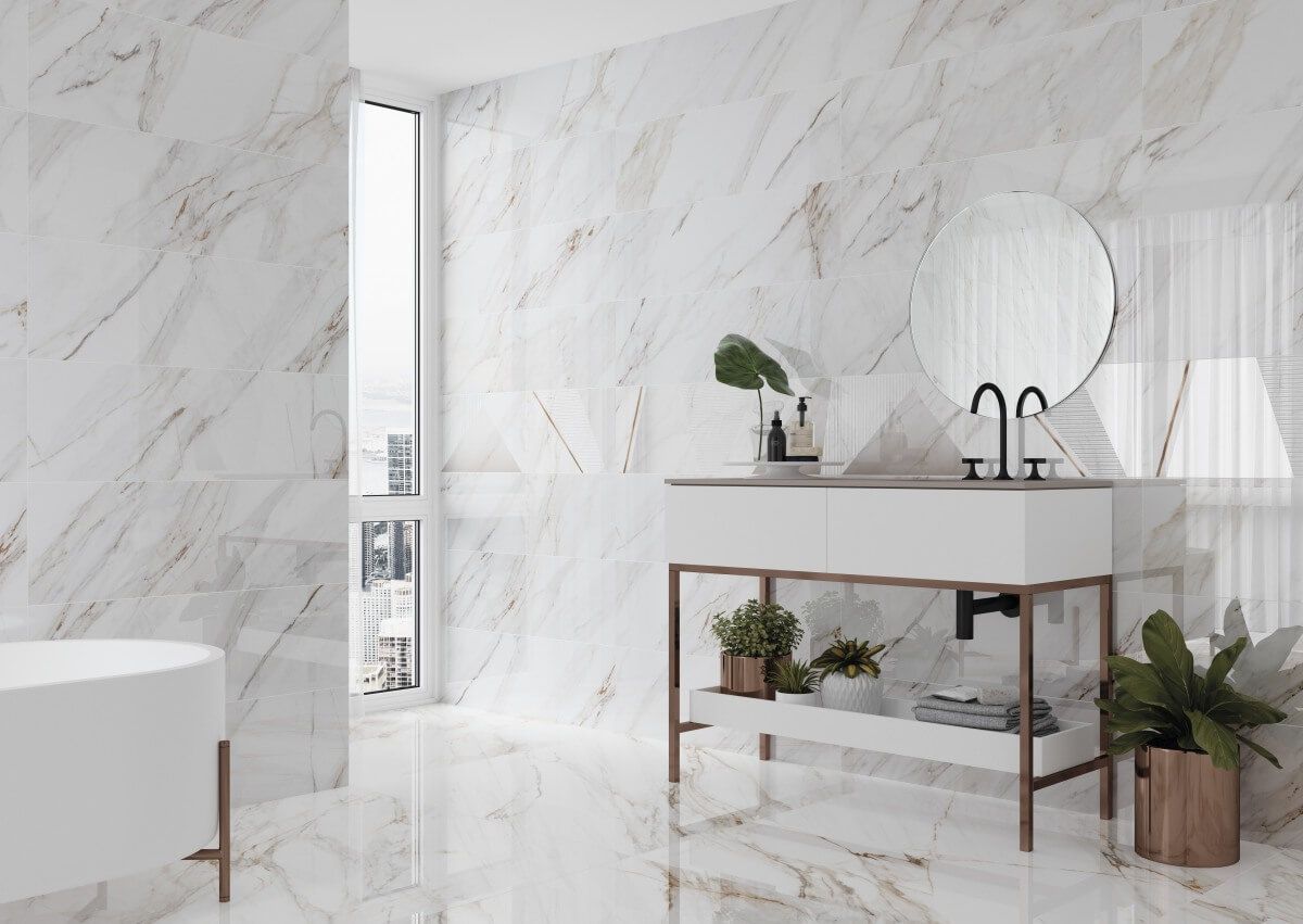 Baño de lujo con paredes y piso de mármol blanco, tocador blanco moderno con detalles dorados y un espejo redondo.