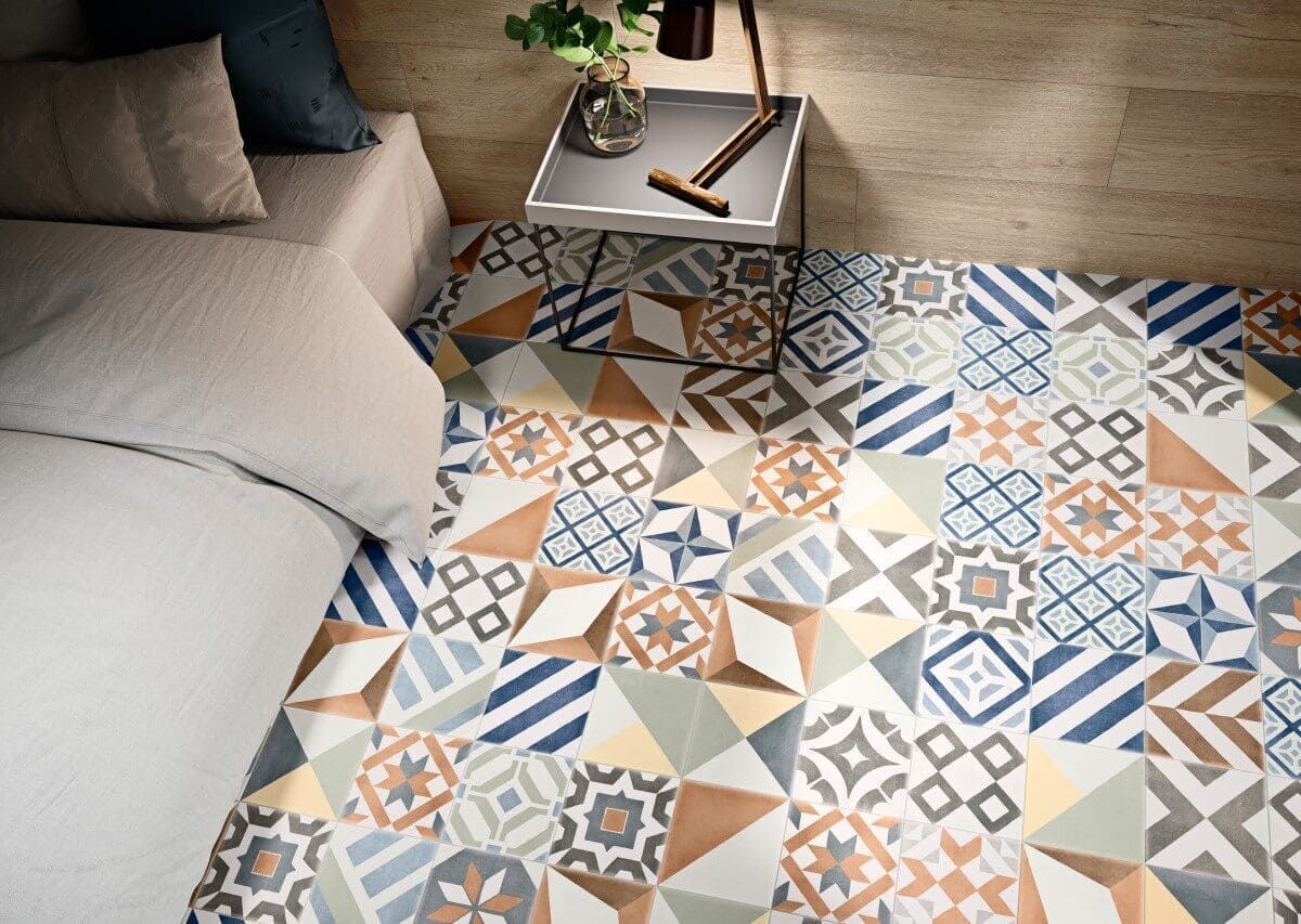 Dormitorio con suelo de baldosas estampadas en azul, beige y naranja. Cama con ropa de cama blanca y almohada azul.