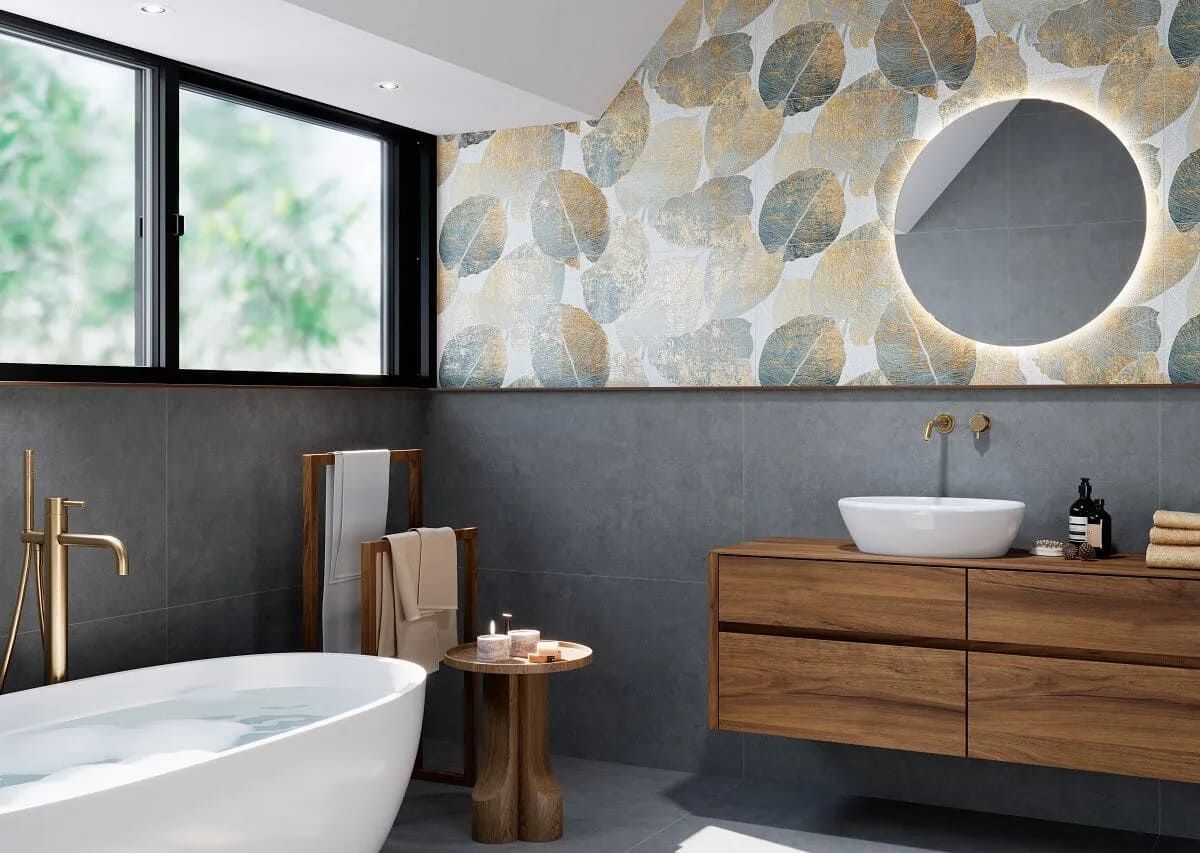 Baño con azulejos grises, tocador de madera, espejo redondo y pared decorativa con diseño de hojas.