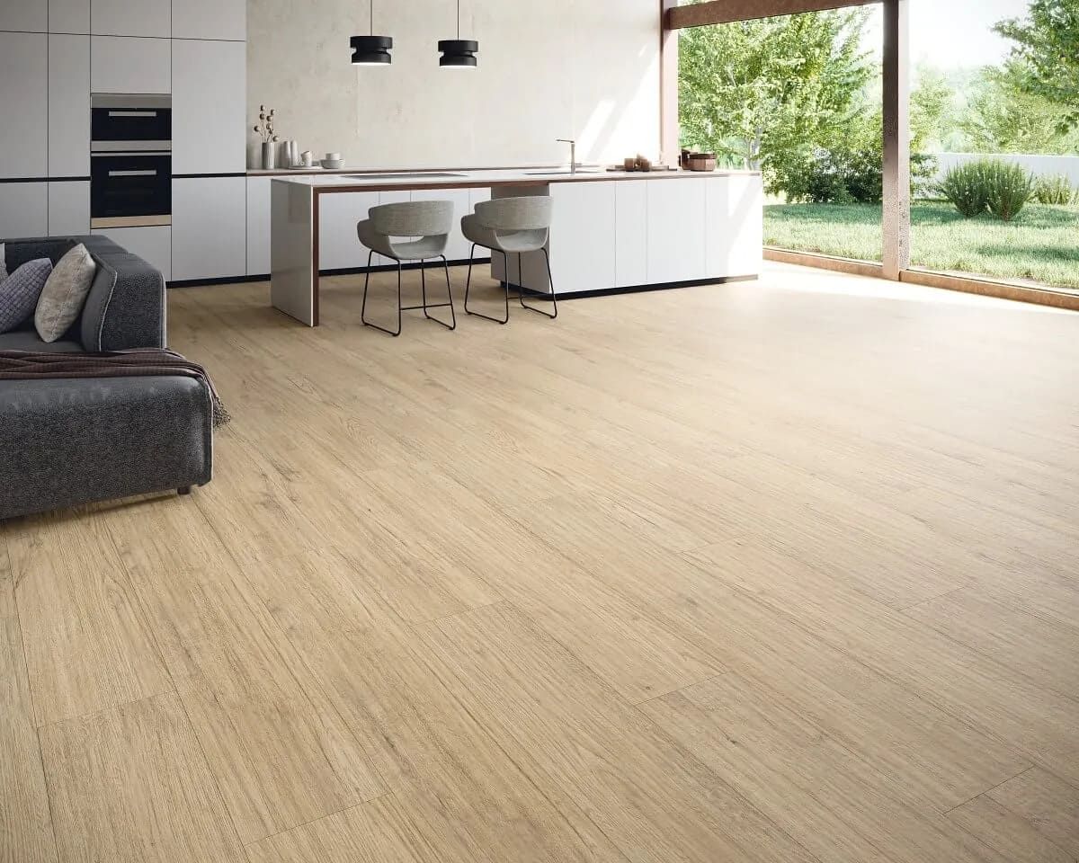 Piso de apariencia de madera clara en una cocina moderna, con gabinetes blancos, isla y puerta abierta a un patio trasero.