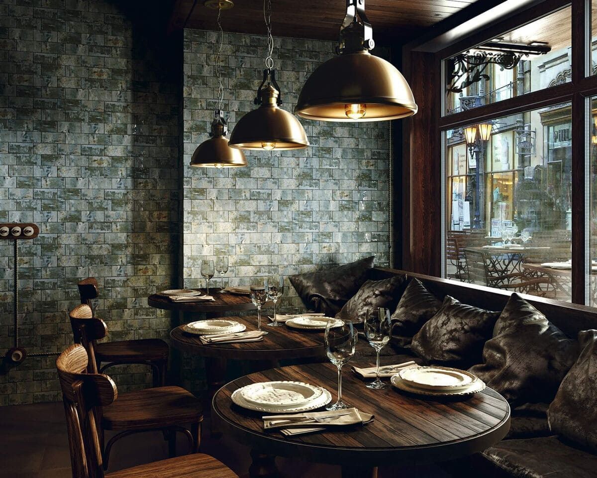 Acogedor interior de restaurante con pared de ladrillo, mesas redondas de madera con platos y lámparas colgantes cerca de una ventana que da a una calle de la ciudad.