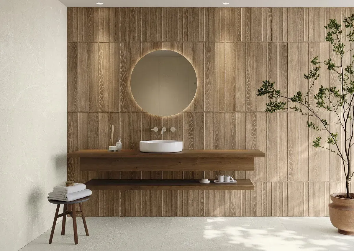 Baño con pared revestida de madera, espejo redondo, lavabo flotante y planta en maceta.