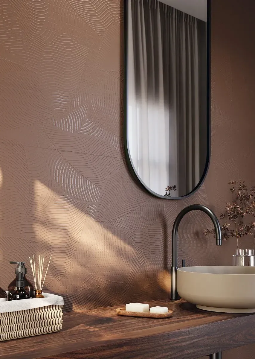 Baño con pared marrón texturizada, espejo ovalado, grifería moderna y lavabo de color claro.