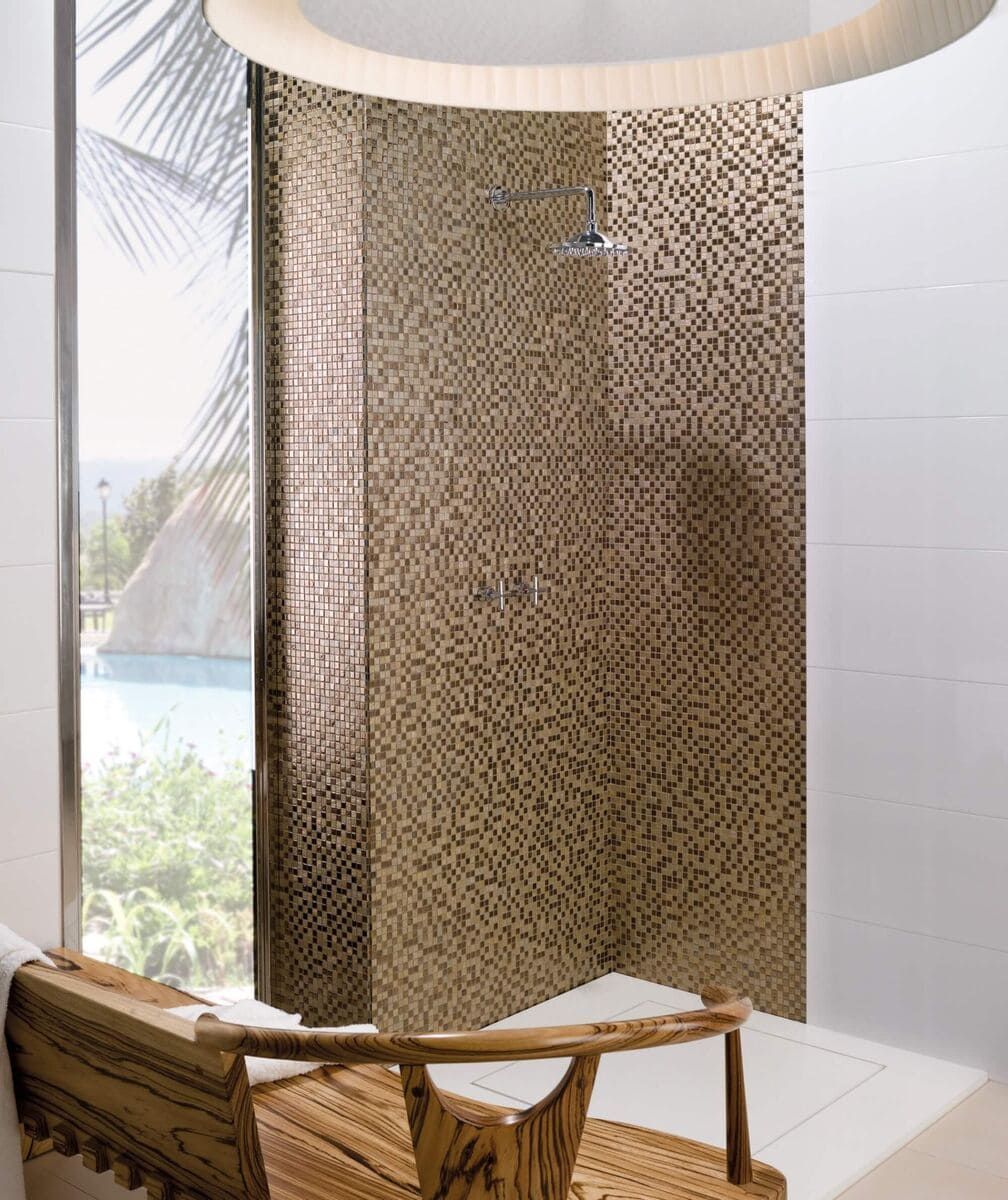 Ducha con pared de mosaico y vistas tropicales. Silla de madera y paredes de azulejos blancos.