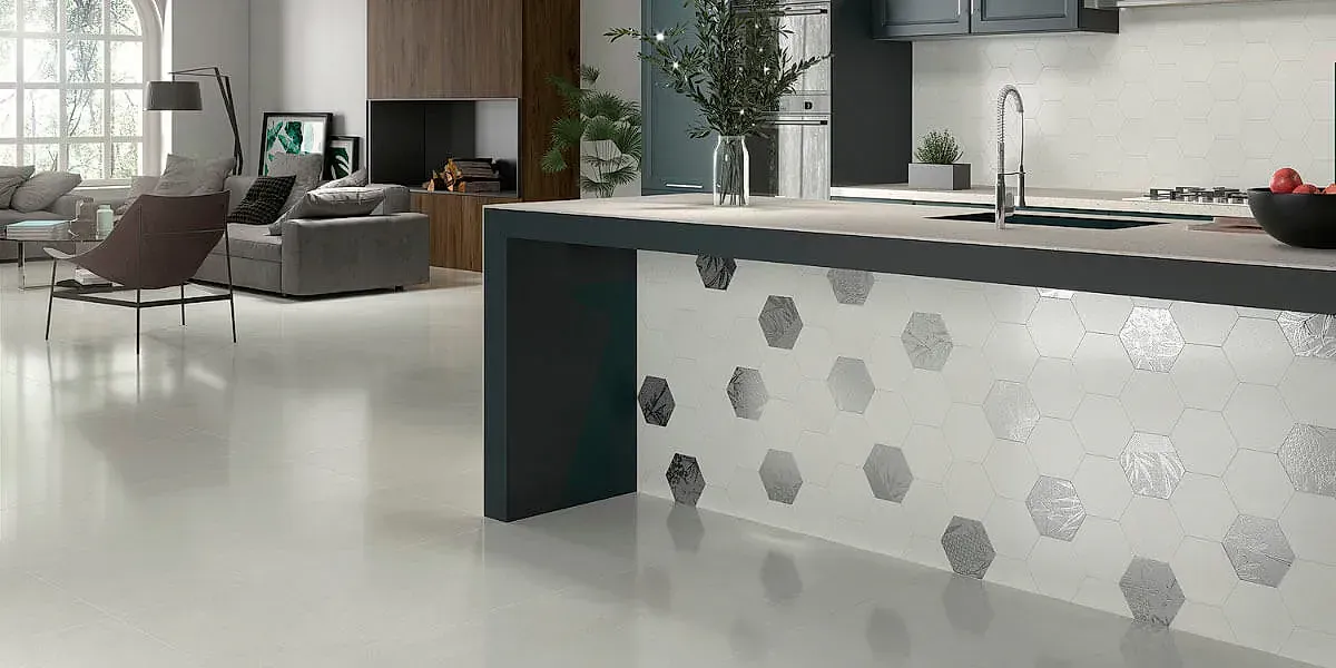 Cocina moderna con encimeras blancas y salpicadero de azulejos geométricos. Isla gris con sala de estar abierta al fondo.