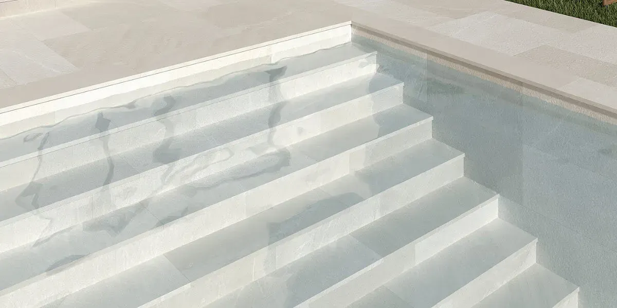 Escaleras que conducen a una piscina de agua cristalina. Azulejos blancos, marco de piedra.