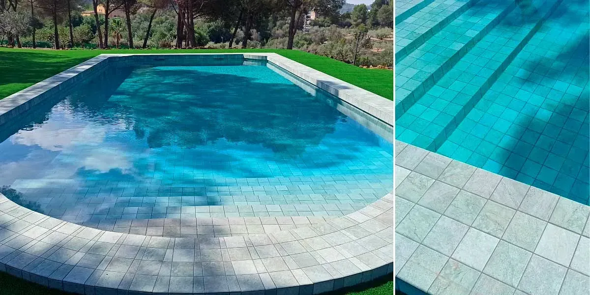 Una piscina rectangular de agua azul. Está rodeada de azulejos y rodeada de césped verde. Árboles al fondo.
