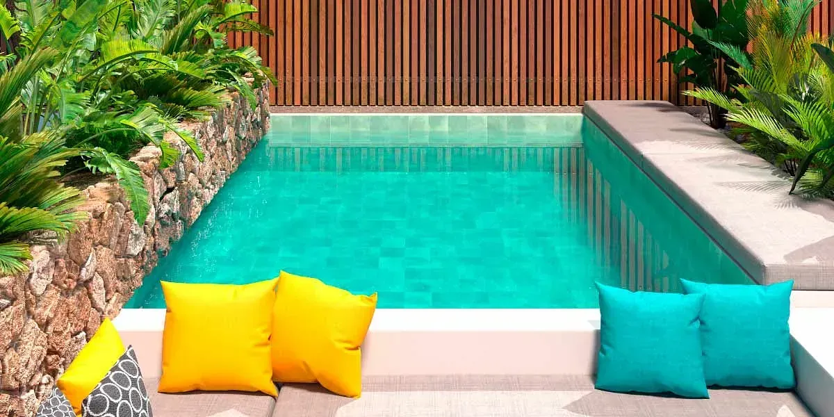 Pequeña piscina de agua turquesa, rodeada de plantas y valla de madera, con almohadas de color amarillo y verde azulado.