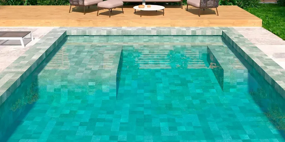 Una piscina rectangular con azulejos de color verde azulado, escalones, terraza de madera y muebles de salón.