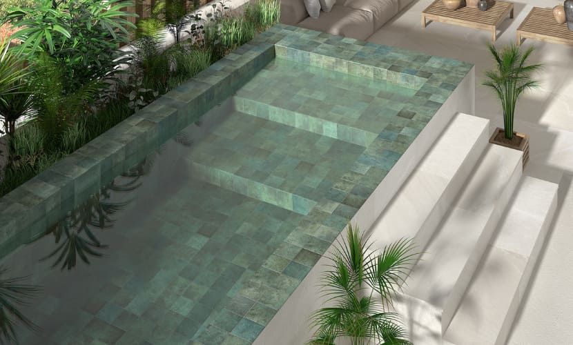 Piscina rectangular con mosaico turquesa, escalones, palmeras y zona de descanso.