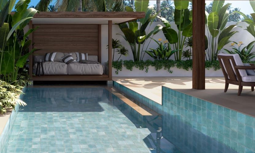 Cabaña junto a la piscina con piscina de azulejos azules, asientos y exuberante vegetación tropical.