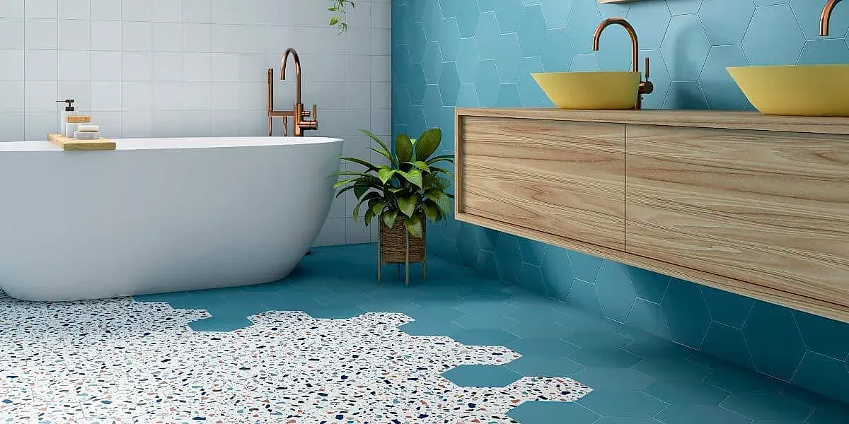 Baño moderno con bañera, tocador de madera, lavabos amarillos y suelo verde azulado con diseño de terrazo.