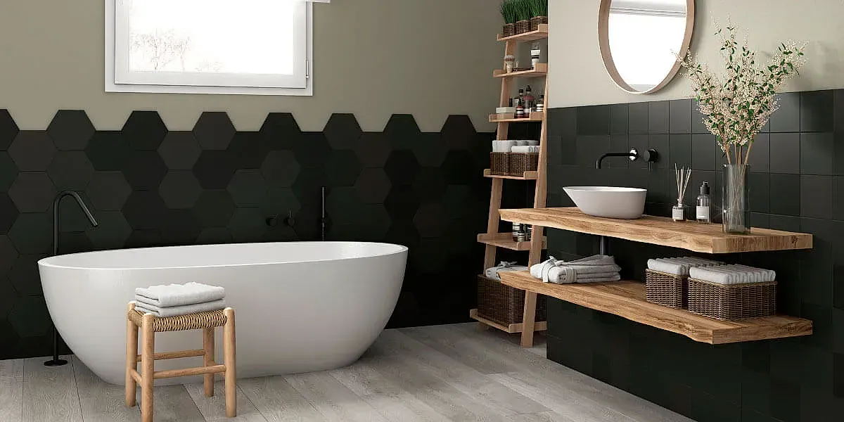 Baño con bañera blanca, azulejos hexagonales negros, estantes de madera y suelo de color claro.