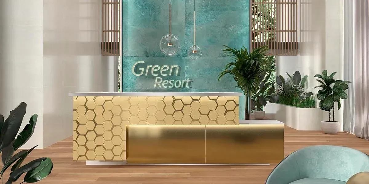 Recepción del Green Resort con un escritorio dorado y plantas. Pared verde azulado y suelo de madera clara.