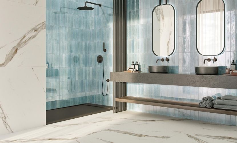 Baño con ducha de azulejos azul claro, tocador de mármol y dos espejos ovalados.