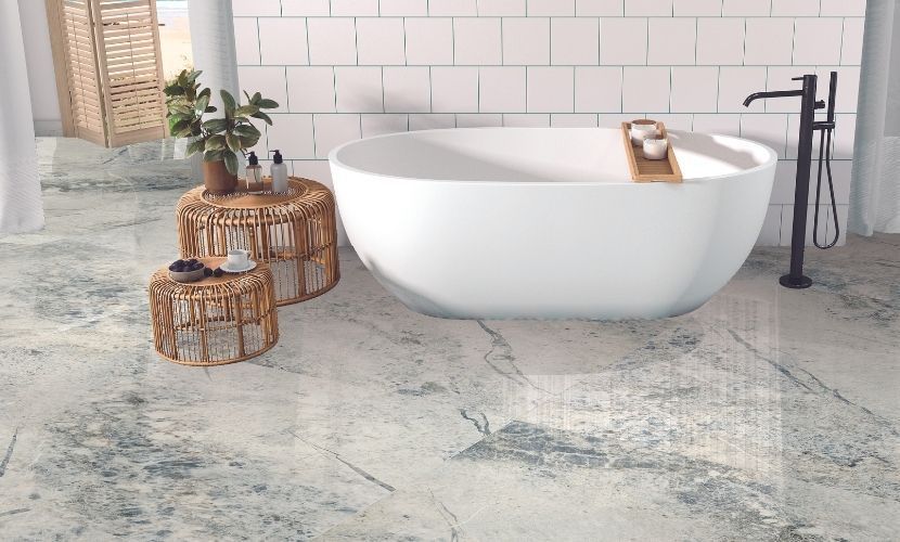 Bañera blanca en un baño moderno con suelo con estampado gris, mampara de madera y mesitas con plantas.