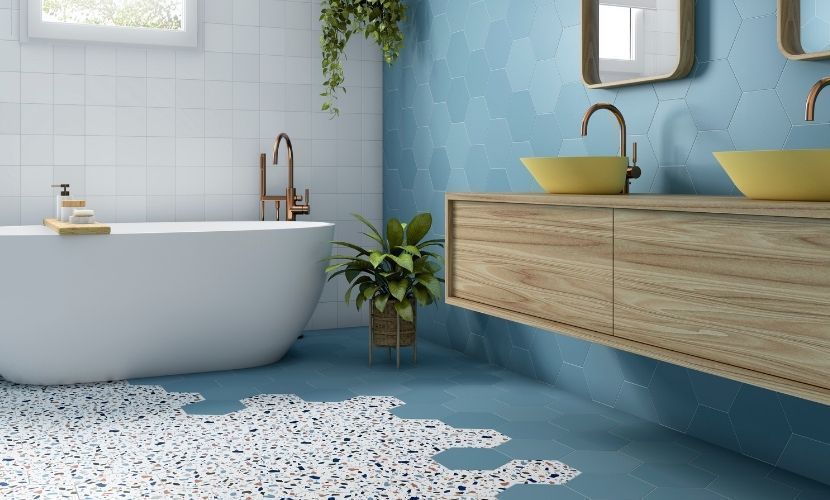 Baño con bañera blanca, tocador de madera clara con lavabos amarillos, pared con acento azul y piso de terrazo.