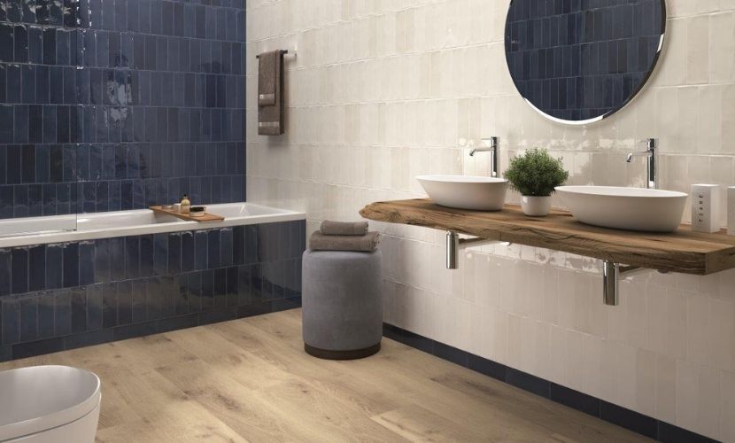 Baño con paredes de azulejos azules y blancos, piso de madera y tocador de madera con dos lavabos.