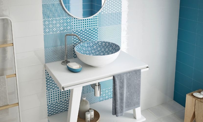 Baño con lavabo blanco, lavabo con estampado azul, pared con detalles de azulejos azules y toalla.