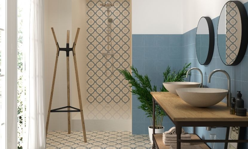 Baño con azulejos estampados, lavabos dobles, tocador de madera, perchero y espejos circulares.