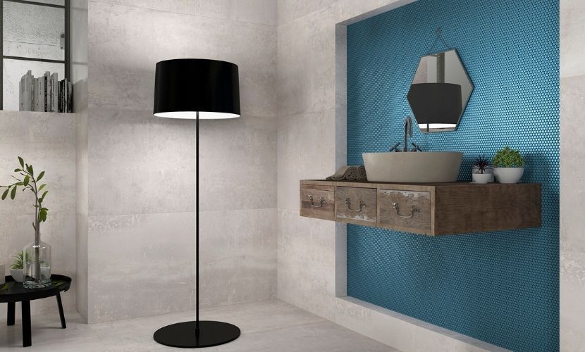 Baño con pared decorativa de mosaico azul, tocador de madera flotante y lámpara de pie negra.