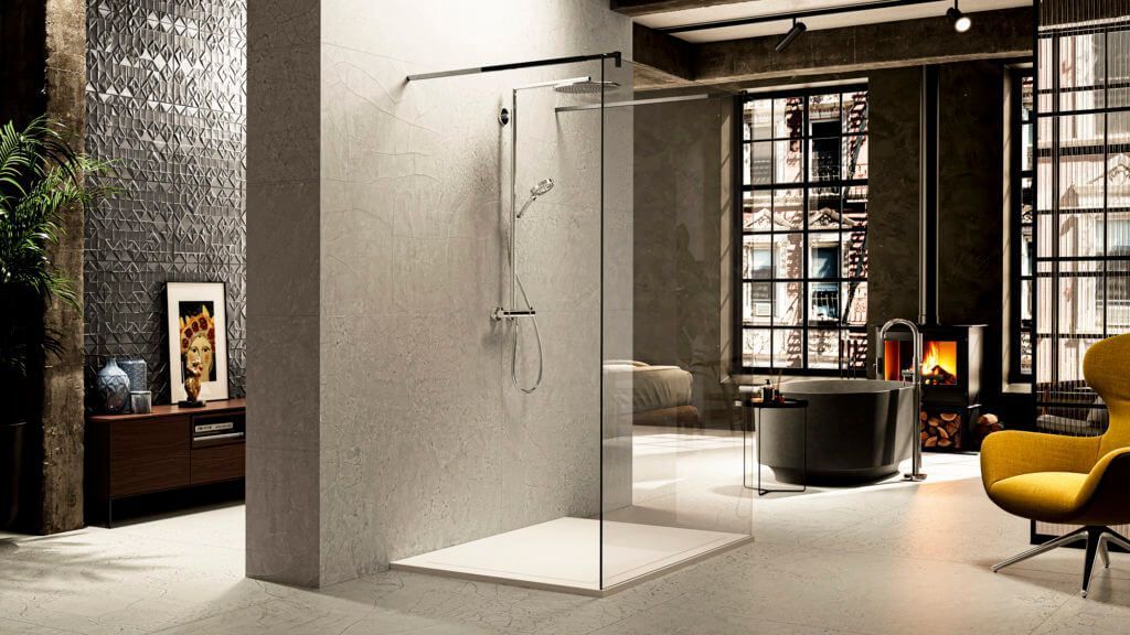 Baño moderno con ducha de cristal, paredes grises, decoración oscura y sillón amarillo.