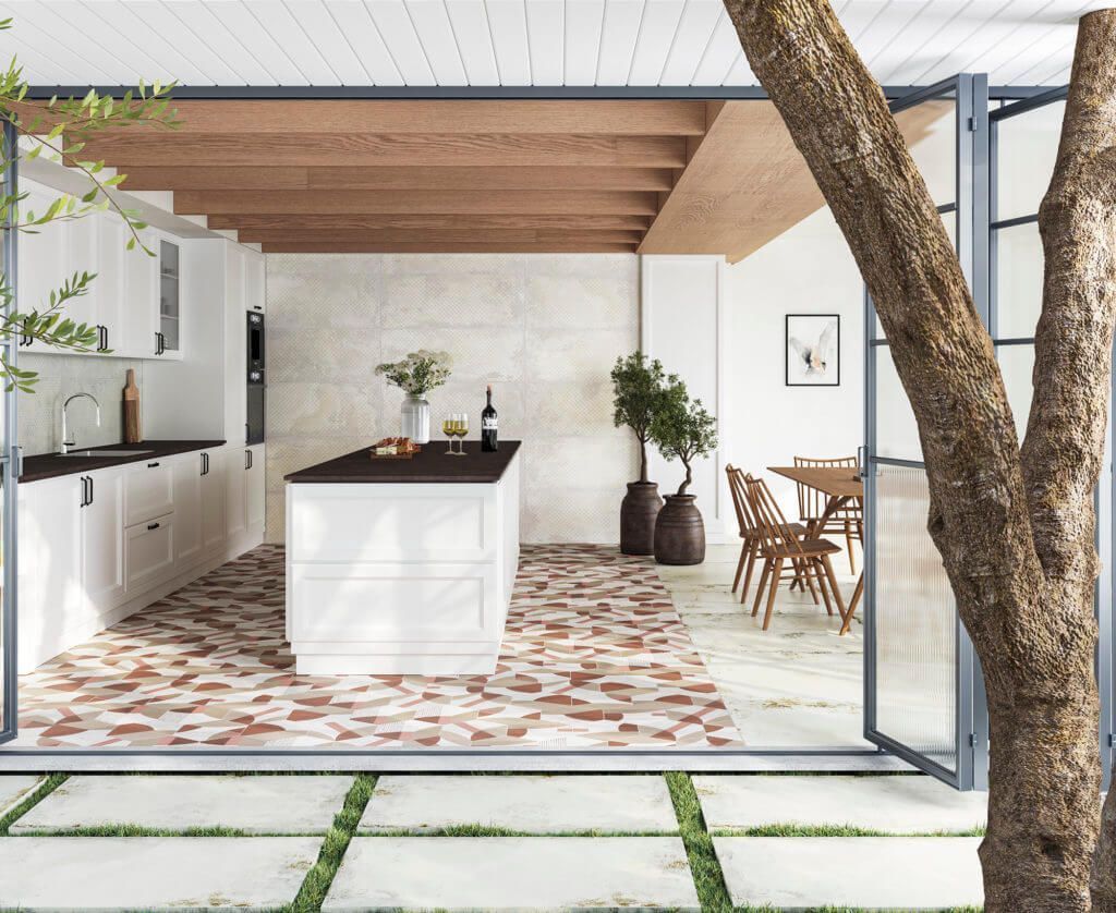 Cocina al aire libre con gabinetes blancos, isla oscura, piso de ladrillo y puertas de vidrio plegables, con comedor.