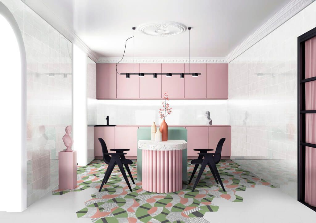 Cocina rosa y blanca con suelo geométrico. Armarios rosas, mesa redonda, sillas negras y elementos decorativos.