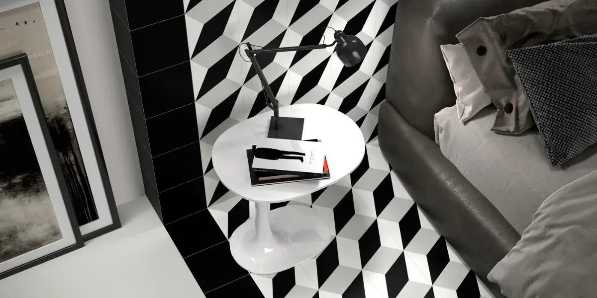 Dormitorio con pared con estampado geométrico en blanco y negro, mesa blanca, lámpara y cama con almohadas.