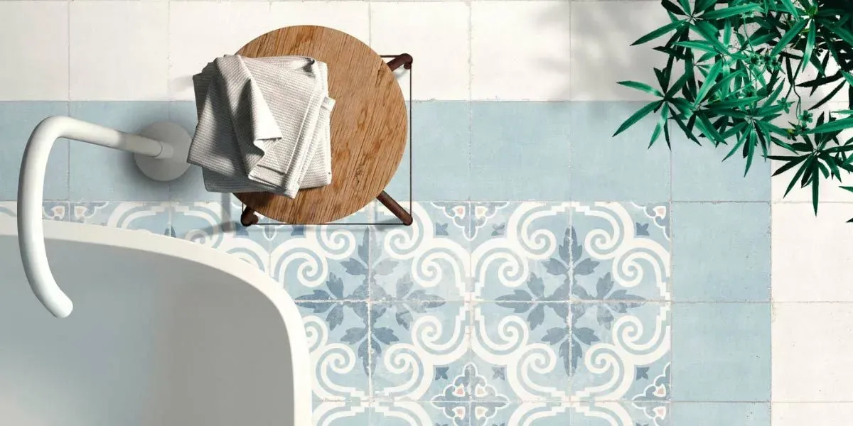 Vista aérea de un baño con bañera blanca, azulejos azules estampados y una mesita con una toalla. Planta verde.