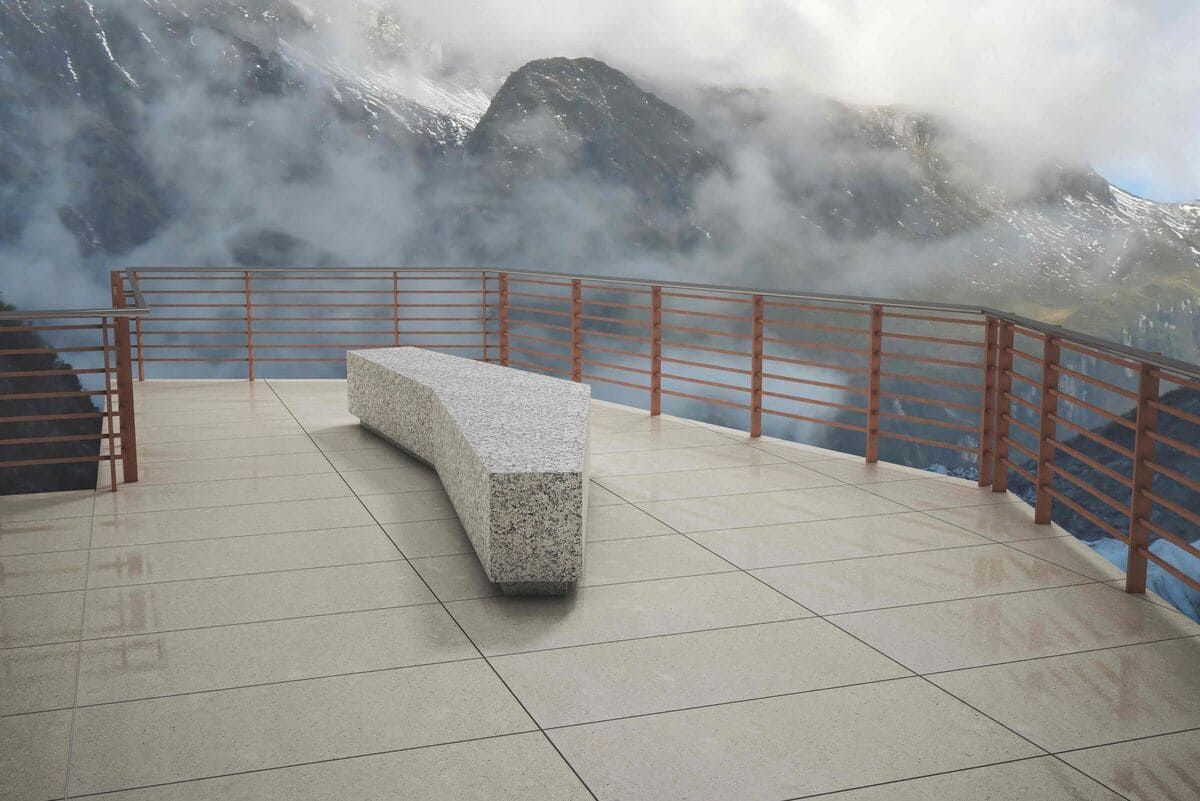 Plataforma de observación al aire libre con un banco de hormigón curvado y barandilla, con vistas a un paisaje montañoso brumoso.