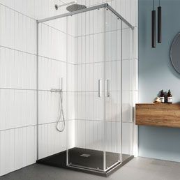 Mampara de ducha de cristal en un baño con paredes de azulejos blancos y suelo oscuro.