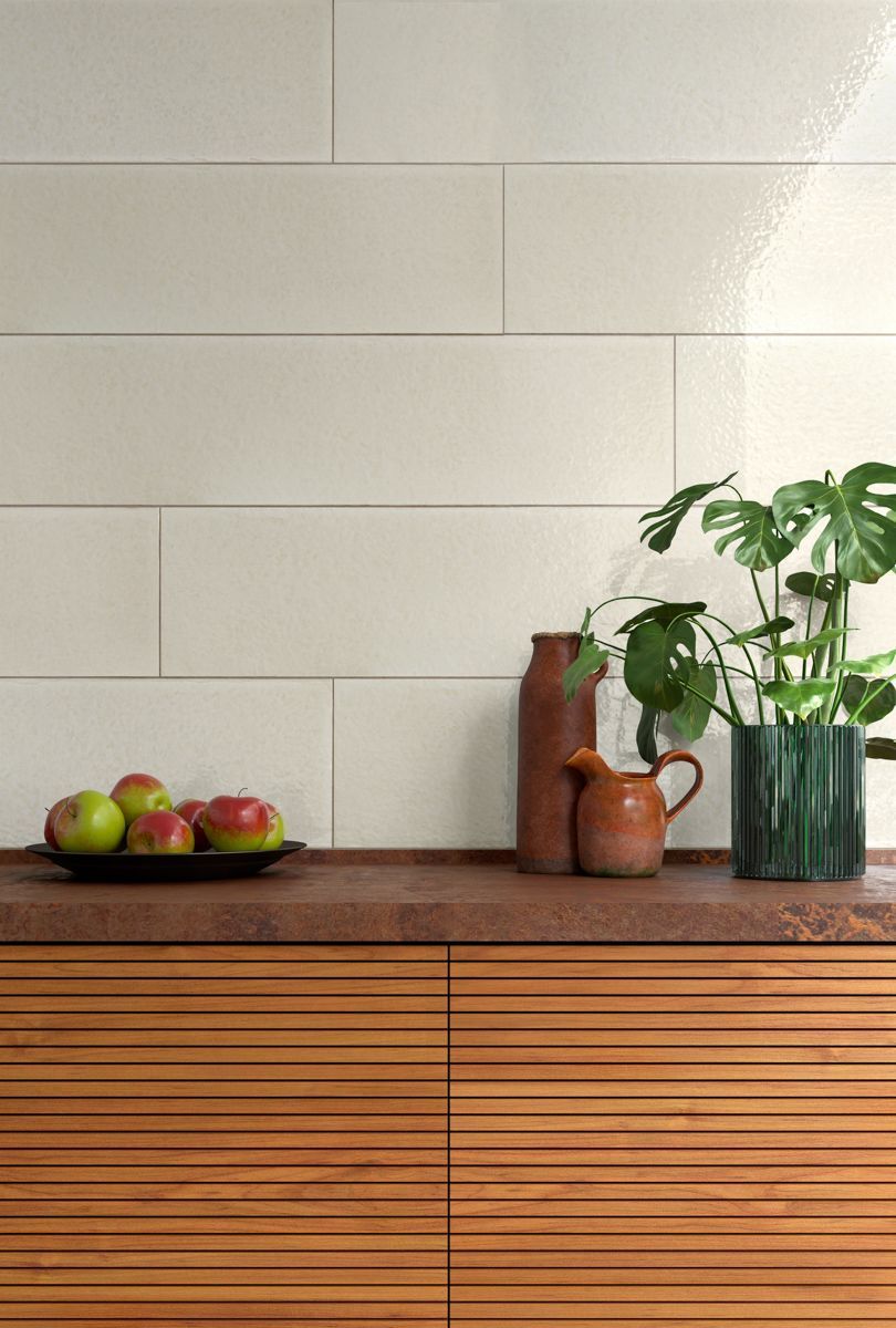 Pared de azulejos color crema con armarios de madera. Frutas y plantas sobre una encimera de madera con cerámica marrón.