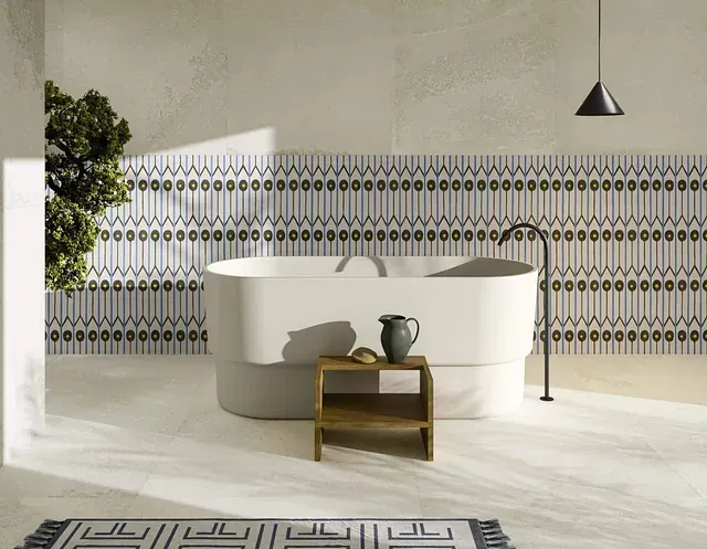 Baño con bañera blanca, pared de azulejos estampados, taburete de madera y grifo negro.
