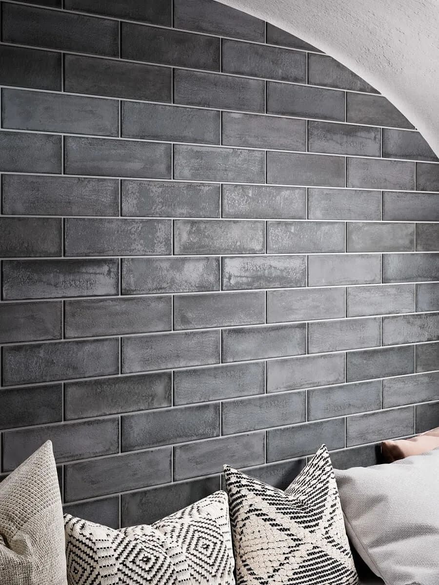 Pared de azulejos de ladrillo gris con lechada plateada, cojines en primer plano.