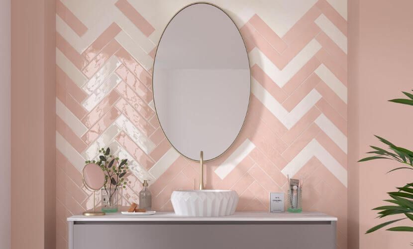 Pared de baño con azulejos en espiga de color rosa y blanco, espejo ovalado, lavabo y tocador.