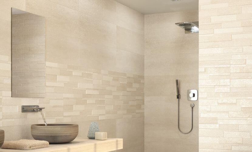 Baño con paredes de azulejos beige, cabezal de ducha y lavabo con cuenco de madera.
