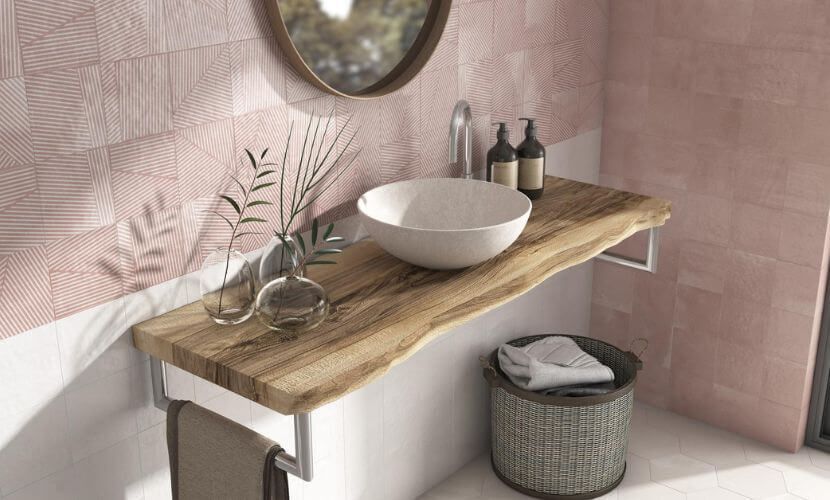 Baño con tocador de madera, lavabo blanco, pared de azulejos rosas y espejo redondo.