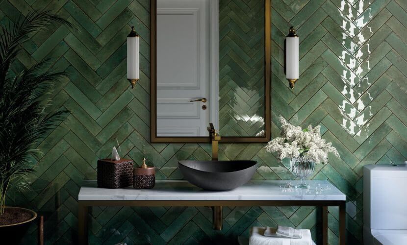 Baño con azulejos verdes, lavabo de mármol, lavabo oscuro, espejo con marco dorado y apliques.