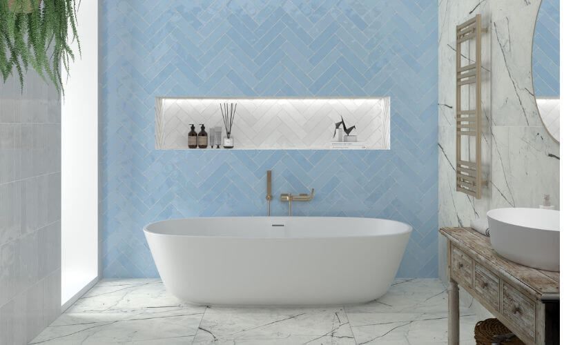 Baño con azulejos azules, bañera blanca y estantería con elementos decorativos.