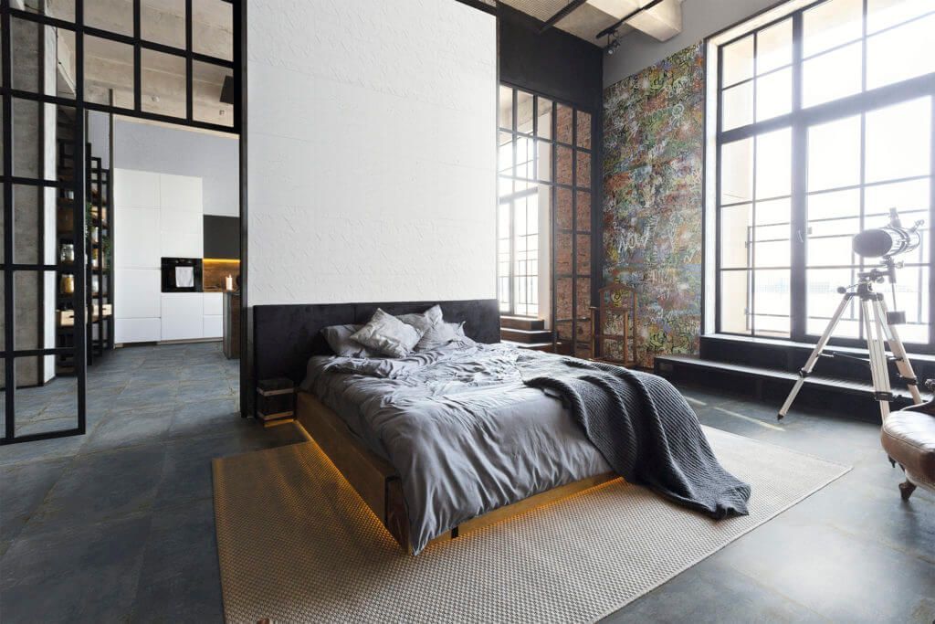 Dormitorio moderno con cama plataforma, grandes ventanales y mamparas de metal y cristal de estilo industrial.