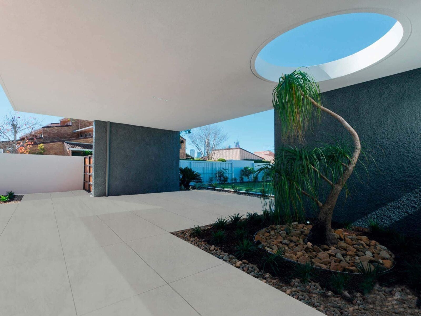 Moderno patio exterior con árbol, grava y tragaluz circular.