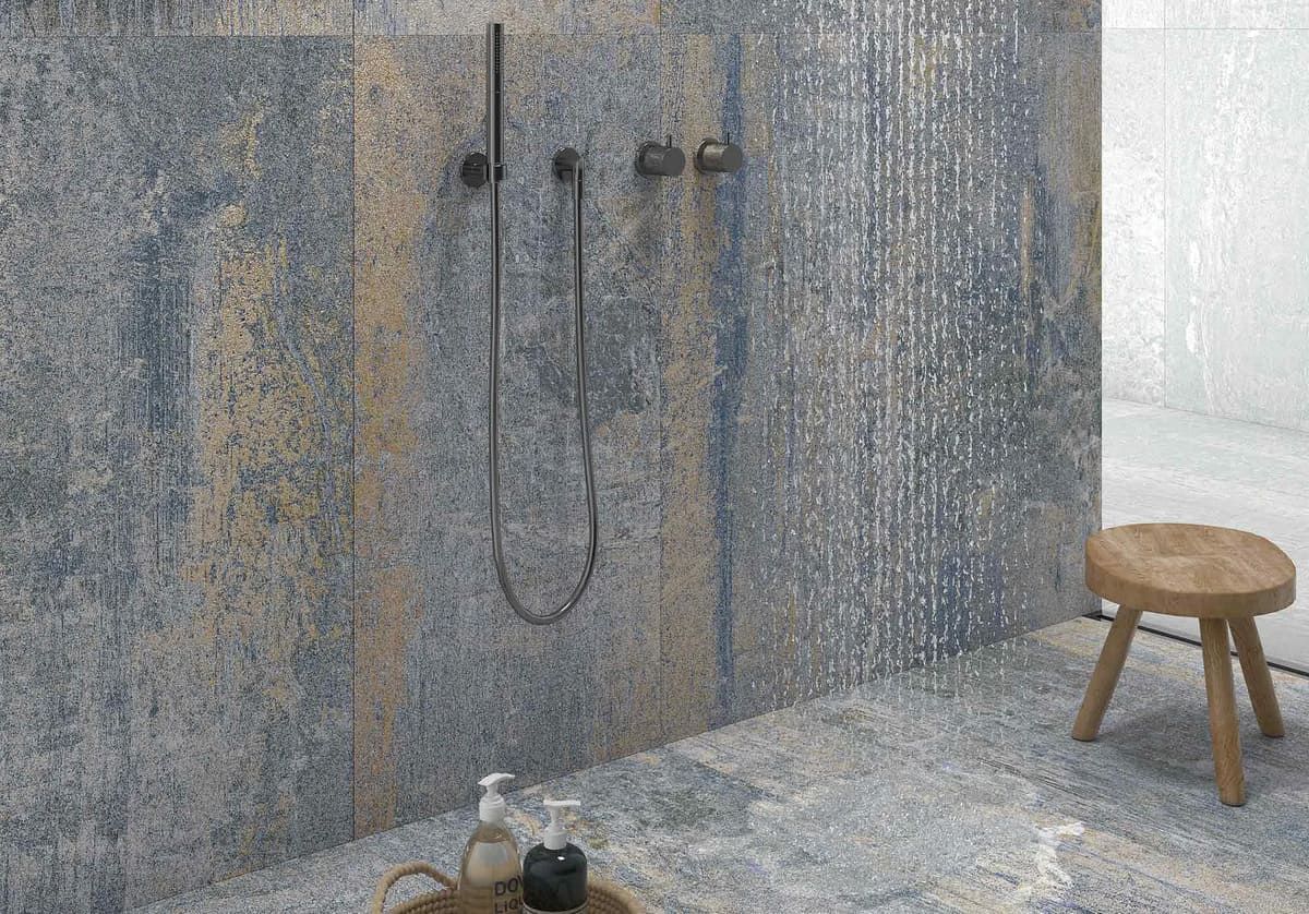 Ducha con azulejos texturizados en azul y beige, grifería negra y taburete de madera.