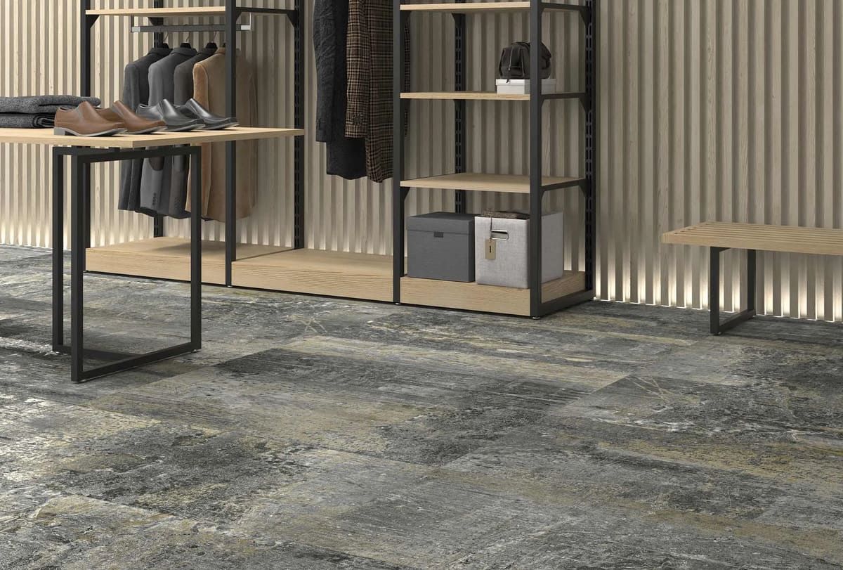 Sala de exhibición de ropa con estanterías de metal, detalles de madera y piso gris texturizado.