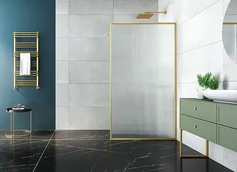 Baño moderno con accesorios dorados, pared verde azulado, tocador verde, piso de mármol negro y ducha grande de vidrio.